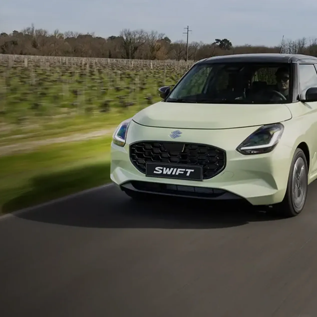 Een suzuki Swift die langs een veld rijdt.